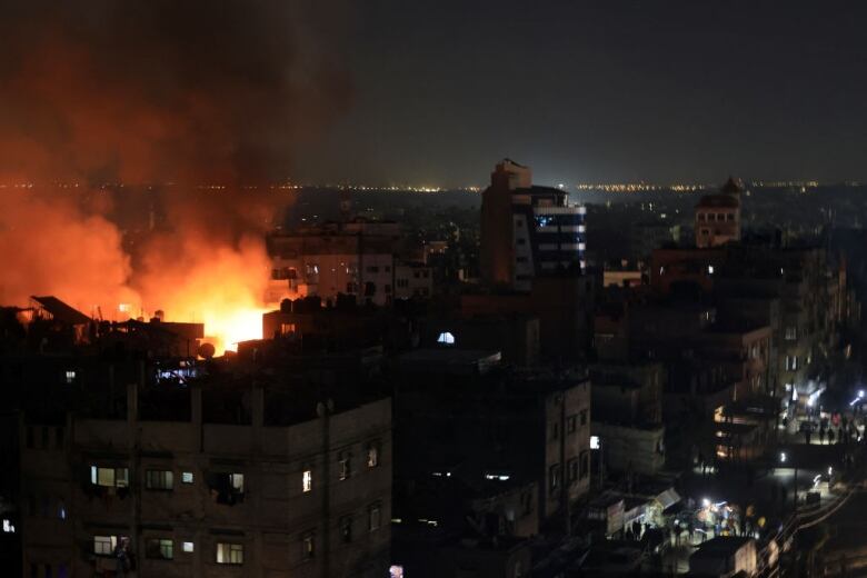 People gather in a street as smoke rises from burning buildings in an adjacent neighbourhood, following an Israeli strike in Rafah in the southern Gaza Strip.