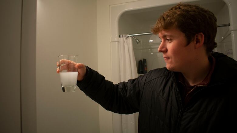 A man holds a cup of murky, white water.