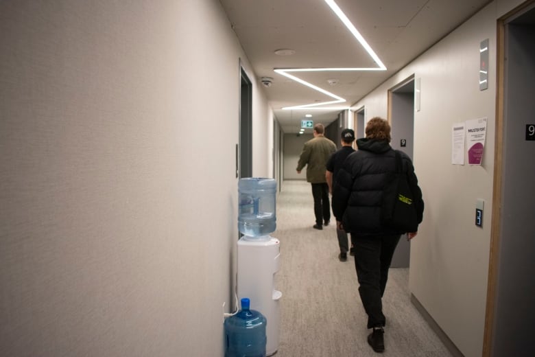 People walk down a hallway with a water cooler in it.