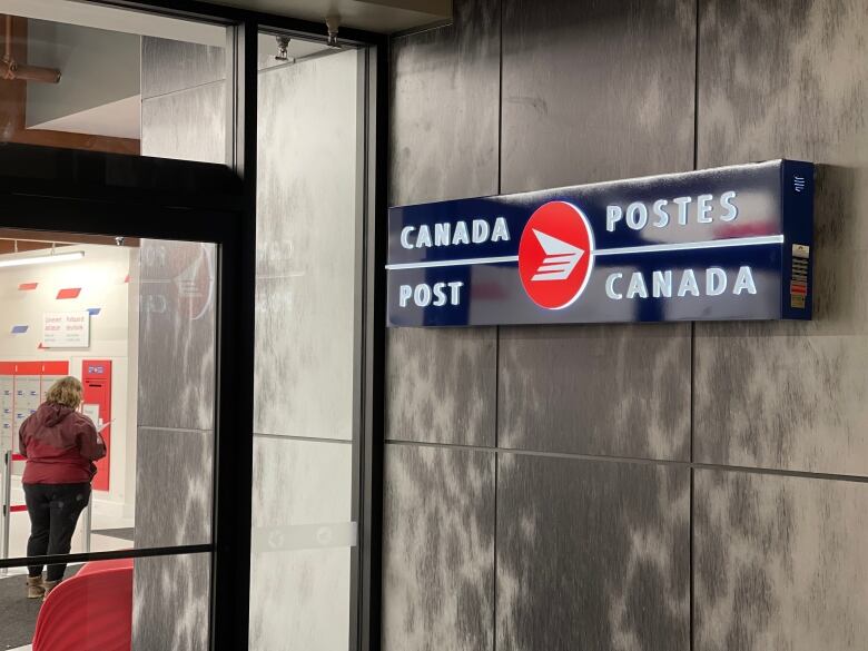 A Canada Post sign is illuminated against a faux seal skin wall, as a woman stands in line inside the new post office.