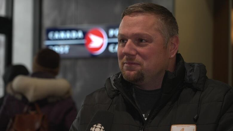 A man with a goatee and a black jacket stands for an interview outside the new Canada Post location in Iqaluit