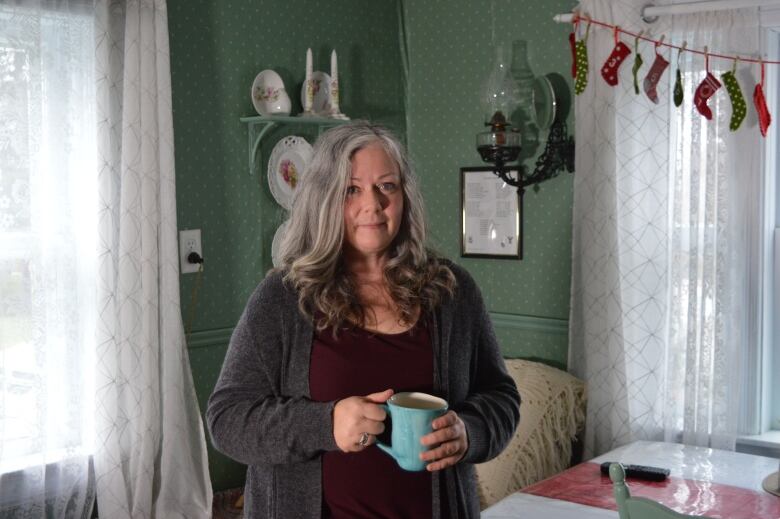 A woman with grey hair sits in front of a kitchen window. 