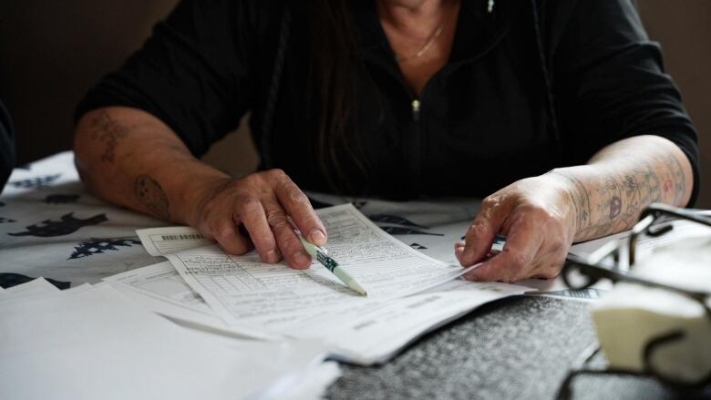 A woman points a pen at a stack of papers. 