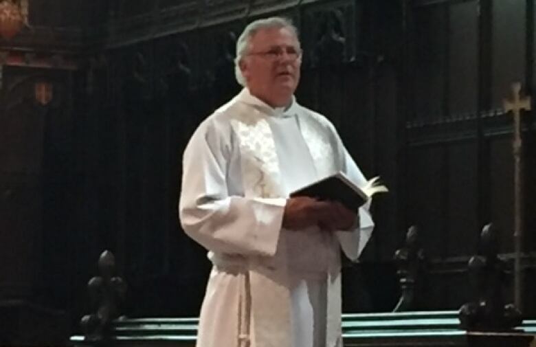 A church minister in a long white traditional robe holding a book.