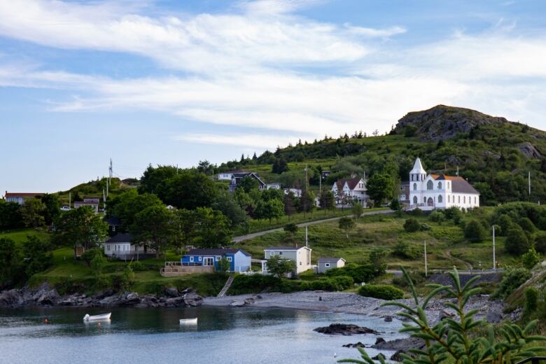 A few buildings and a large white church lie scattered on a hillside in front of a bay.