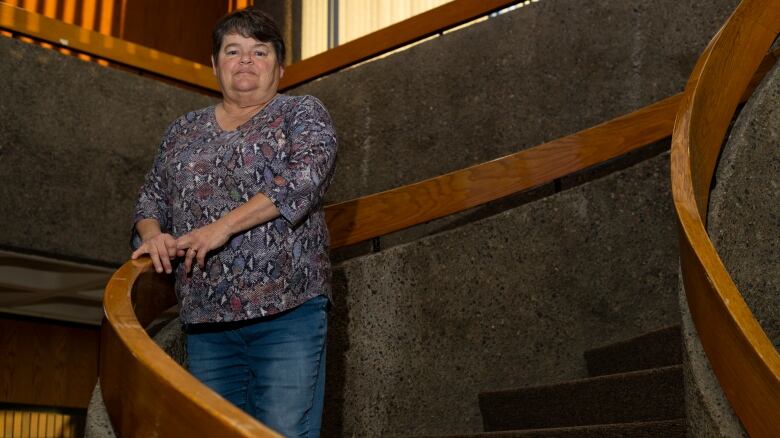 A woman stands on a spiral staircase.