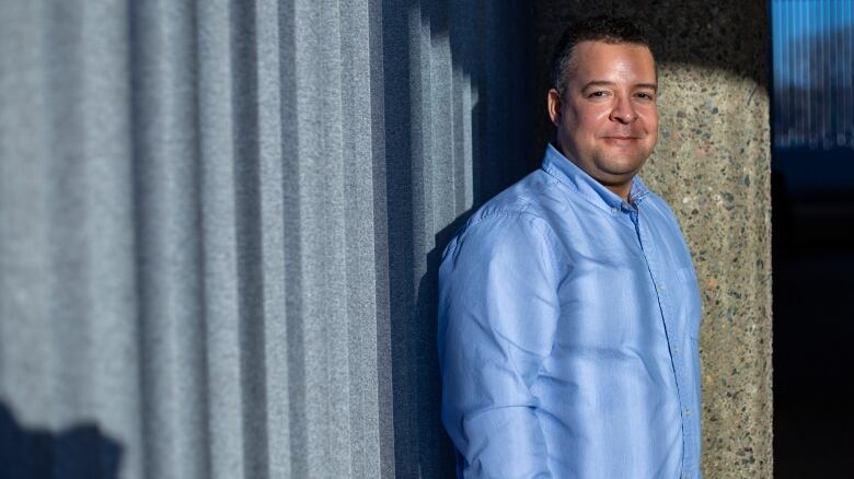 A man stands in front of a cement pillar.