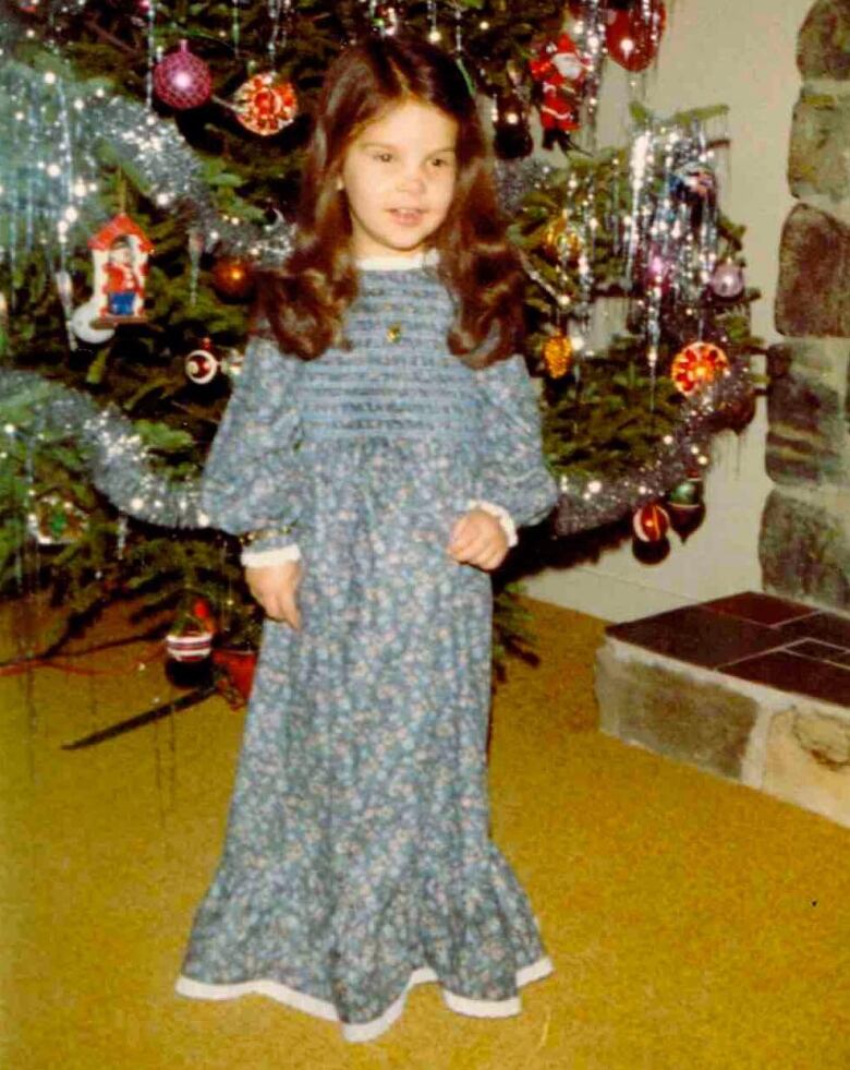 An old photograph of a young girl in front of a Christmas tree.