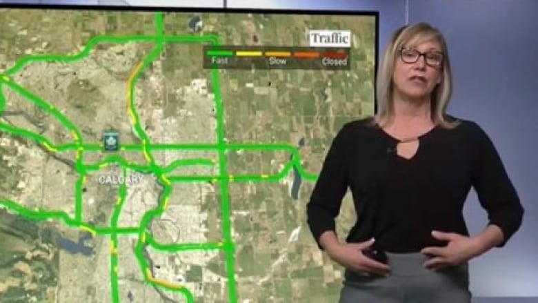 A woman in grey trousers points to her midsection while live on air reporting on traffic in Calgary.