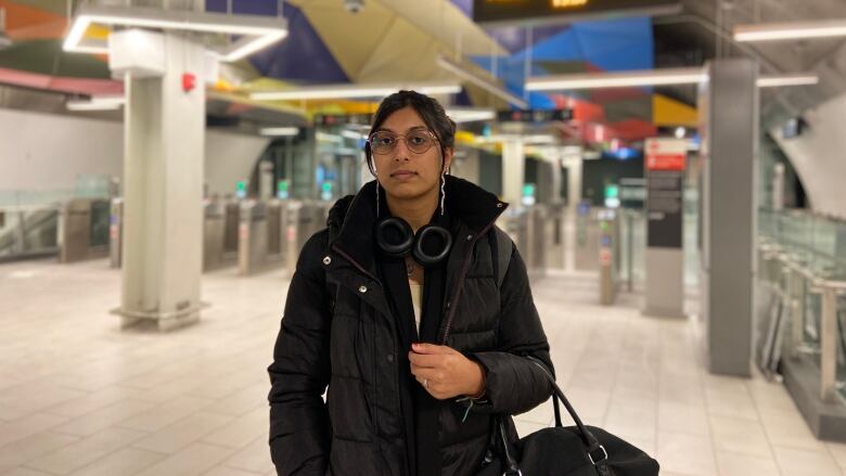 A woman stands in Parliament Station in front of a sign listing LRT arrival times. 