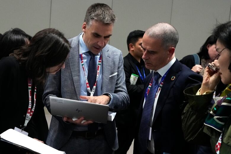 Men in suits gather around a grey HP laptop.