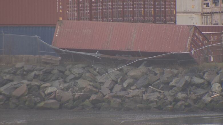 A tipped over shipping container leaning against a broken chain fence.