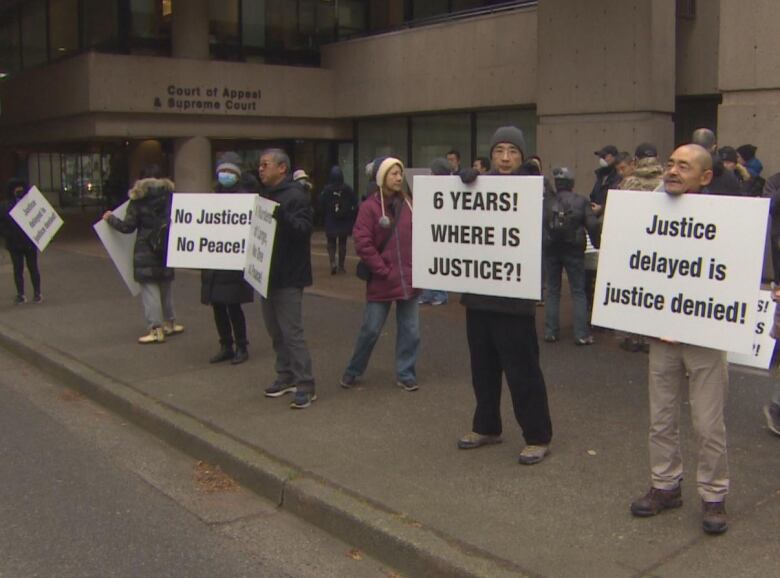 A group of people hold signs on a sidewalk with messages including 