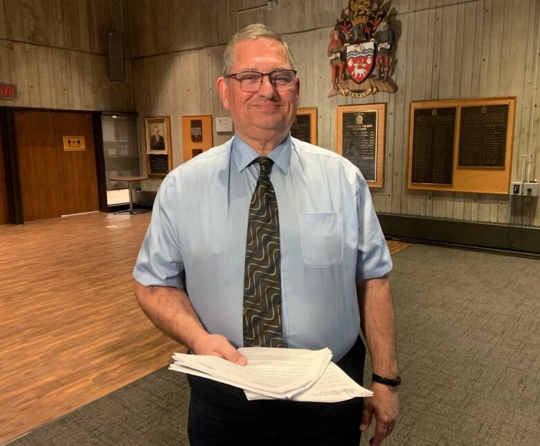 A person wearing a short-sleeved shirt and tie holds a few papers.