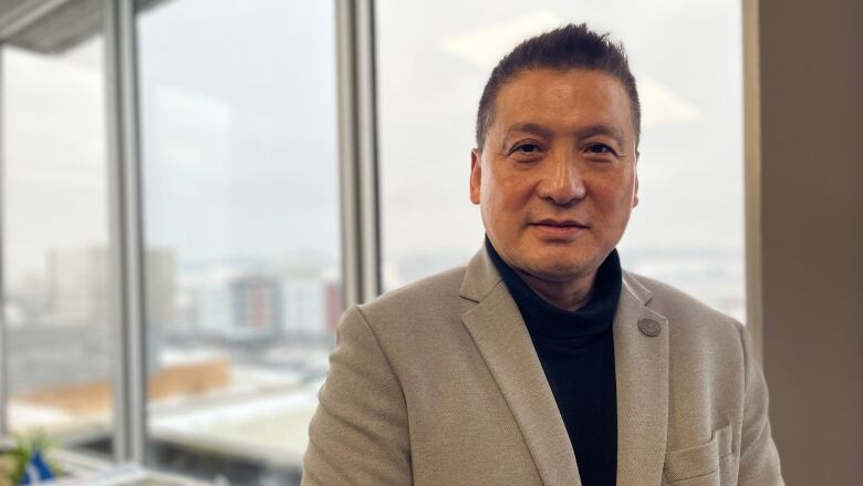 An East Asian man stands by a window overlooking a snowy city.