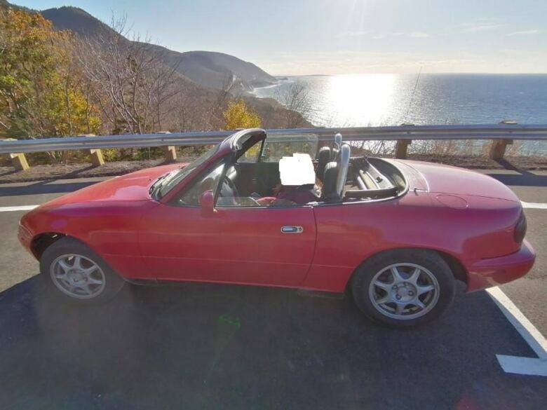 a red car parked by the road next to the ocean.