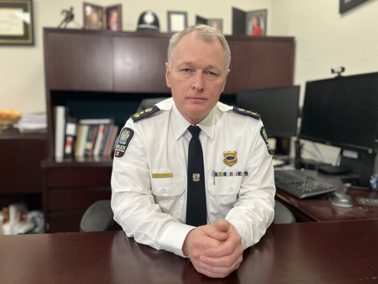 A police chief in his wife shirt and black tie sits at his desk 