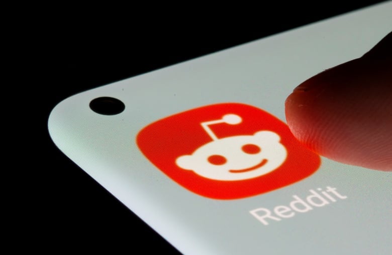 A closeup of a finger tapping a Reddit app icon on a phone screen.