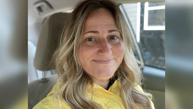 A woman sits inside of a car smiling.