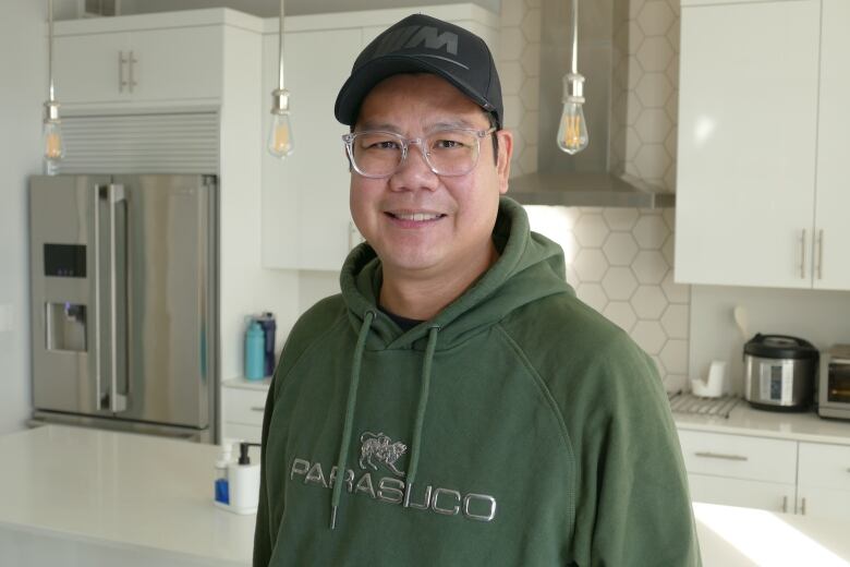 A man with a hat, wearing a green hoodie, smiles.