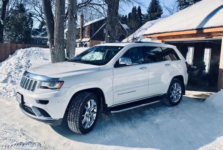 A white Jeep Grand Cherokee SUV is pictured parked in a back lane outside an open garage.