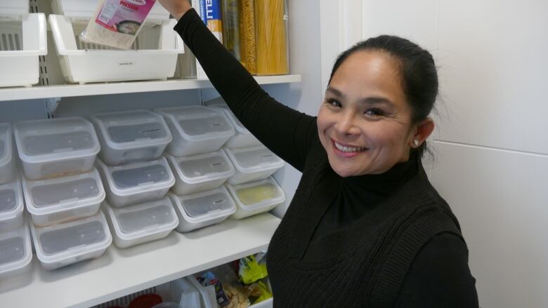 A woman smiles while holding a pack of noodles in her pantry.