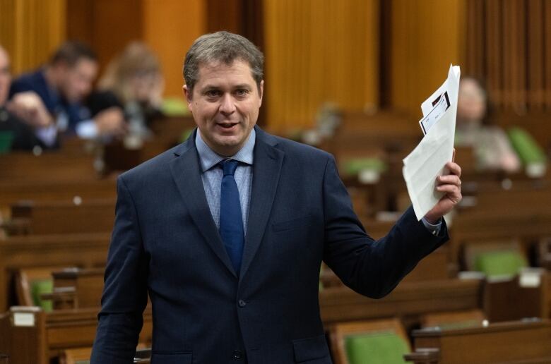 A politician in a blue suit holds a piece of paper in the House of Commons. 