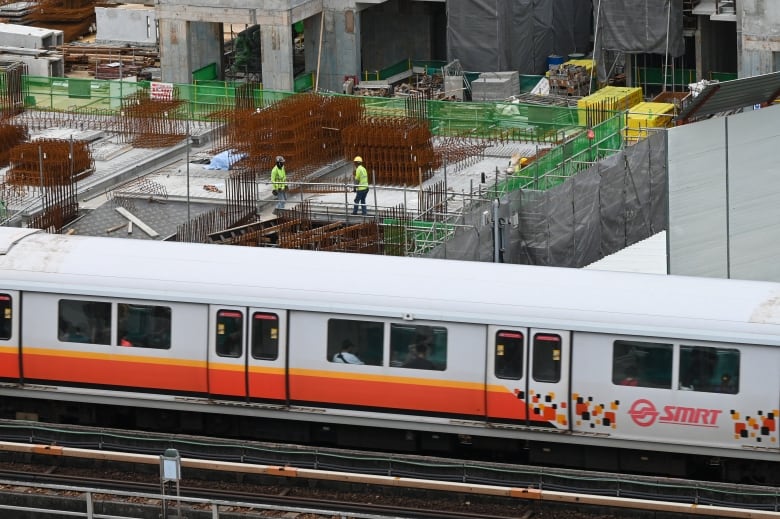 Workers lift building materials while working at a construction site as a mass transit train rolls past. 