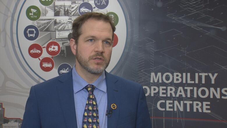 White man in blue suit standing in front of wall that says 