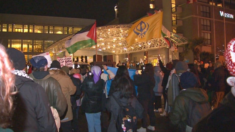 A sea of people and flags in front of a large hotel.