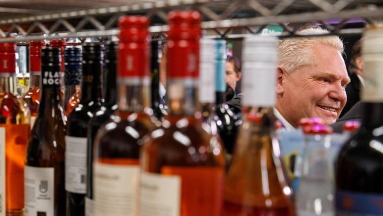 A white-haired man seen through racks carrying bottles of wine at a convenience store.