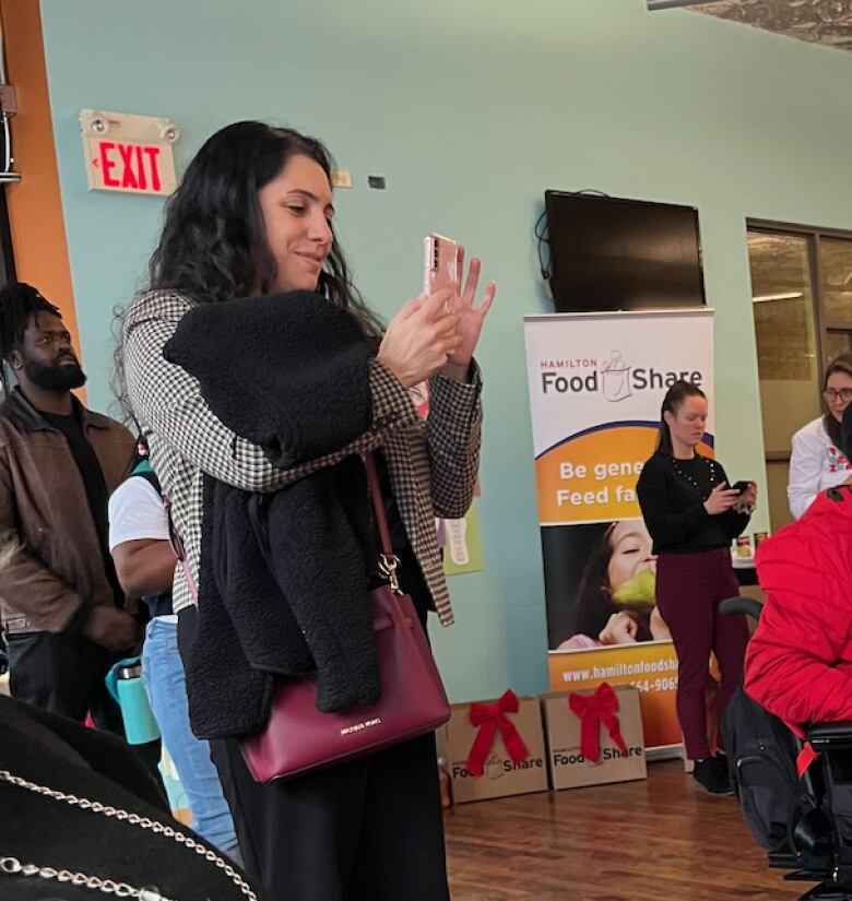 People stand looking at something off camera. A person on the left smiles and holds up her phone. 