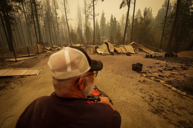 A man looks at the remains of a home as wildfire haze hangs in the air.