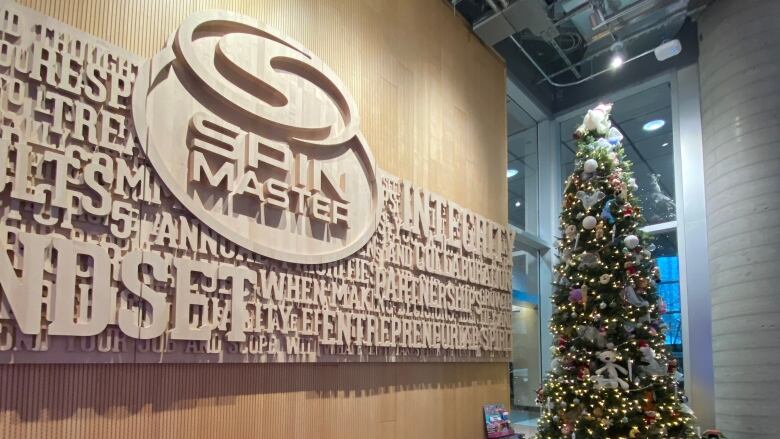 A Spin Master sign is shown in an office lobby with a Christmas tree and toys on a coffee table. 