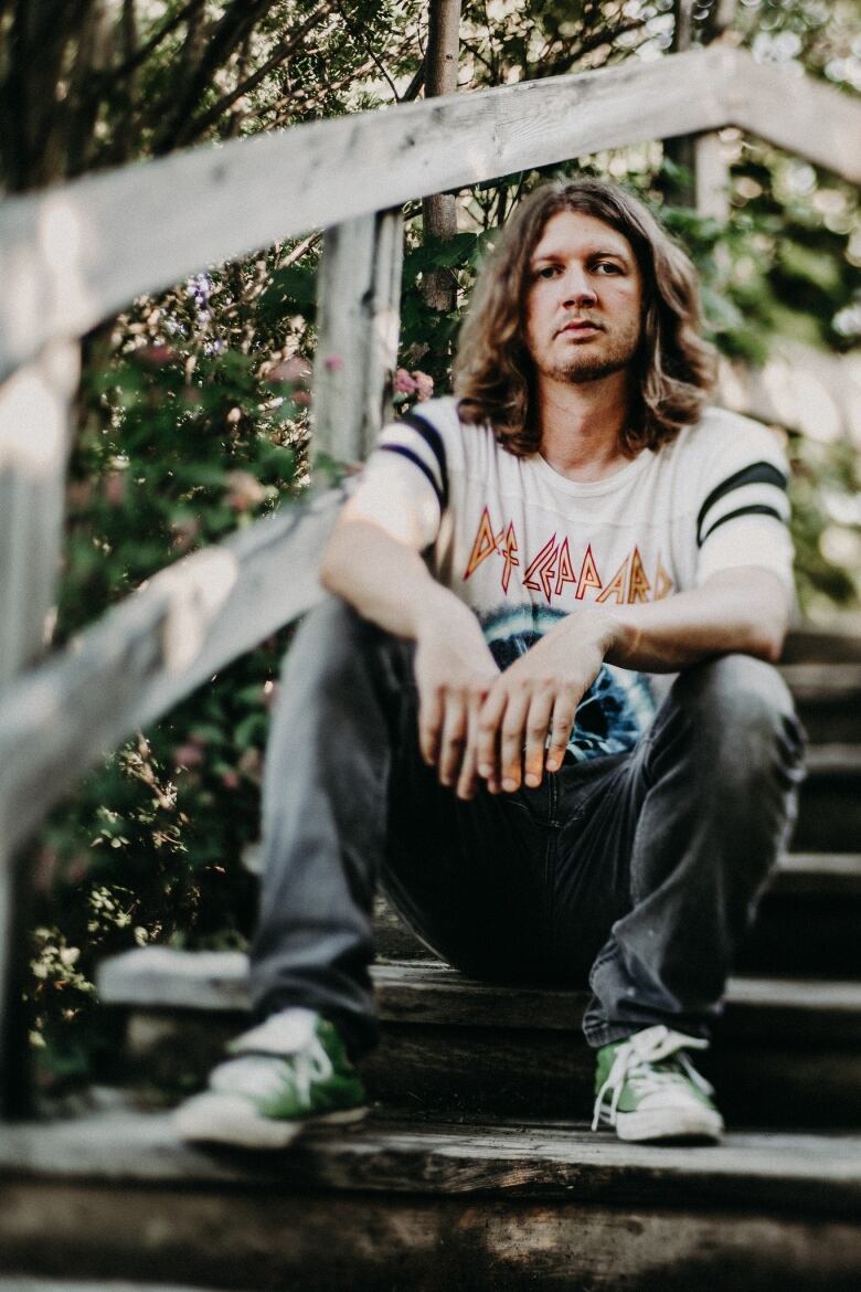 A man in a white Def Leppard T-shirt sits on some outdoor stairs.