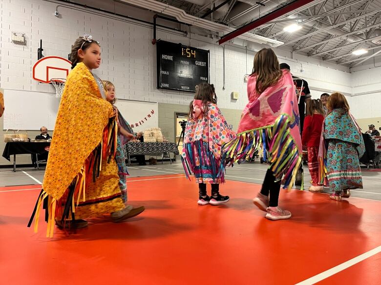 Girls move around the school auditorium in brightly coloured dresses with loose ribbons and tassels. 