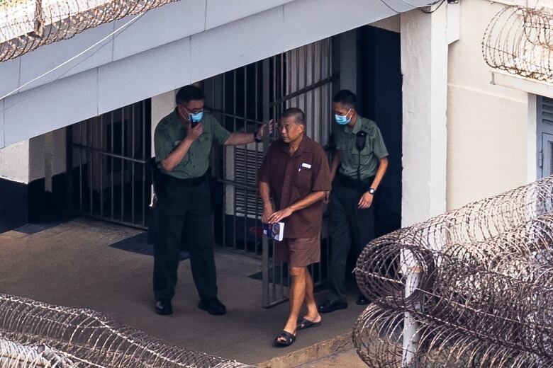 Hong Kong media tycoon Jimmy Lai, centre, walks with two guards in prison.