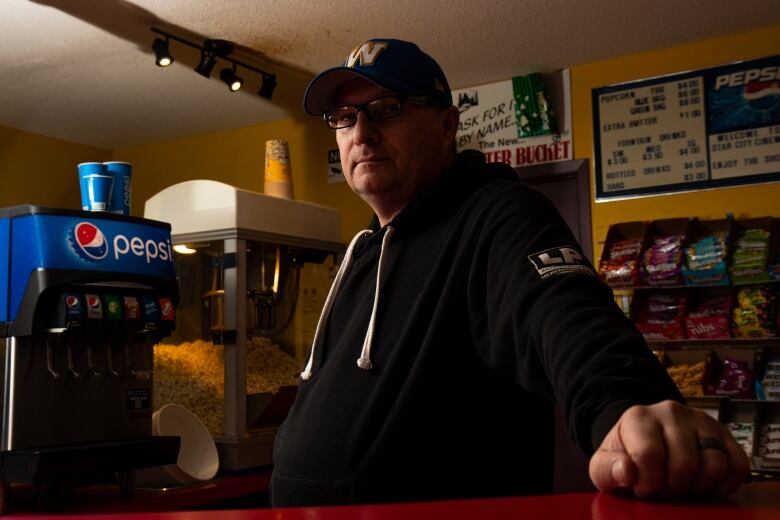 A man stands inside a room next to a popcorn and drink machine.