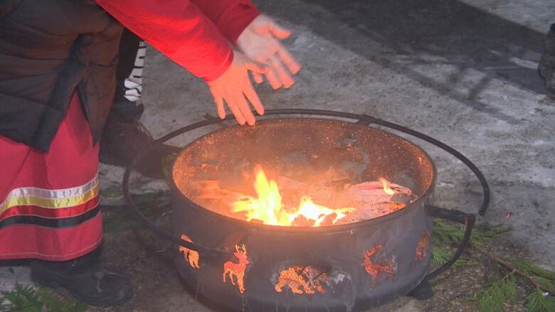 A woman's hands over a wood fire in a metal open fireplace.