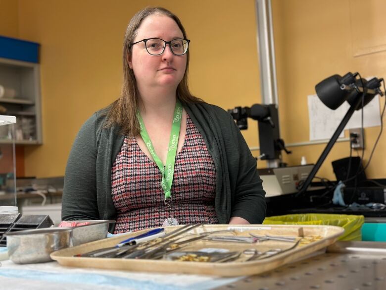 A woman is shown sitting in an autopsy suite with a tray of instruments in front of her.