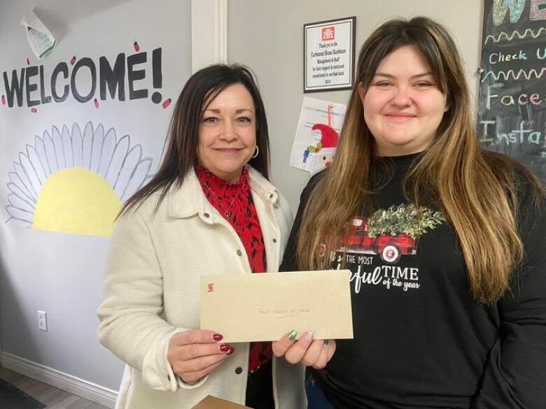 Two woman stand together holding a check and smiling.