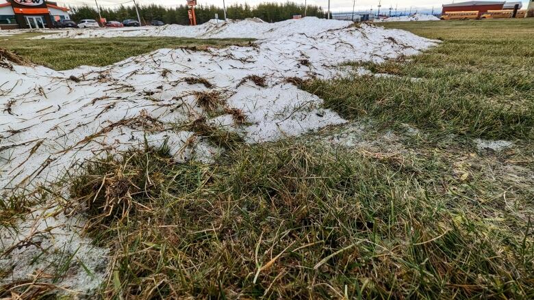 Small patches of snow are sitting on top of a field of green grass. 