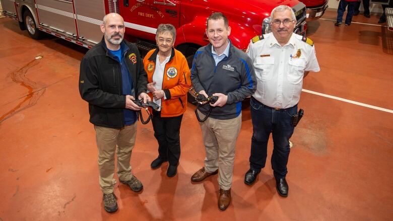 Four people stand in front of a fire truck. Two are holding black mobile radio/walkie talkies