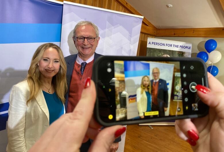 A woman and man pose in a photo together being taken on an IPhone