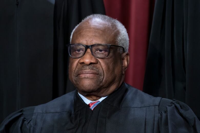 A mustached man with a dark complexion is shown in closeup wearing a robe over a collared shirt and tie.