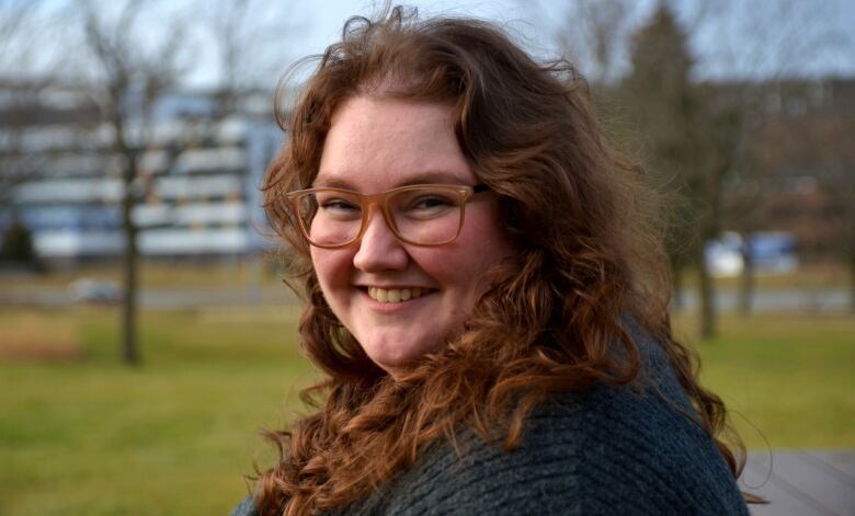 A woman with glasses sitting on a picnic table with trees in the background. 