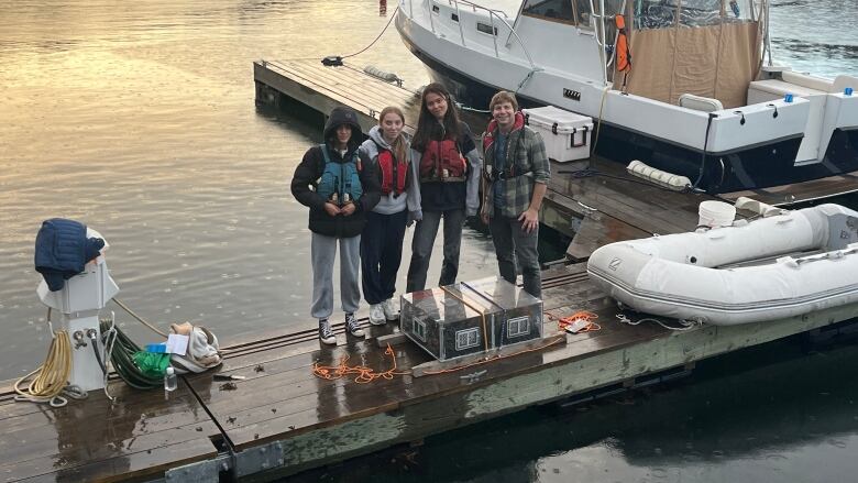 Four people stand on a dock in front of a boat. 