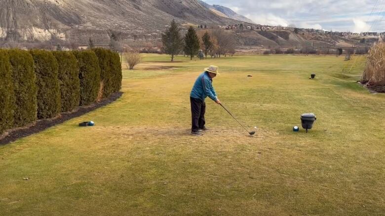 A man in a blue jacket is playing golf on a very green grassy field.