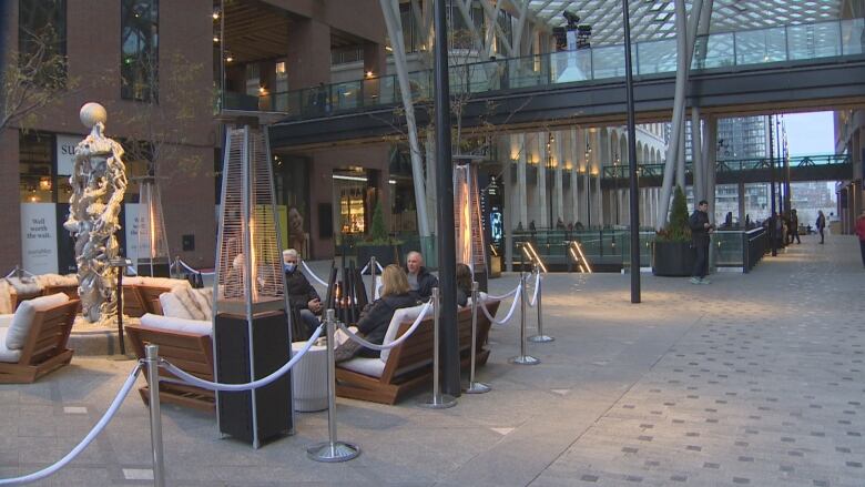 People sit near a fire at an outdoor mall.