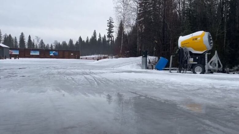 A soggy field is barren with a yellow snowmaker machine sitting idly in the back. 